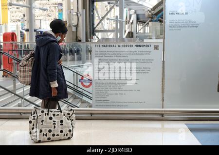 London, Großbritannien, 22.. Juni 2022. Eine Frau hält inne, um die Informationstafel des neuen Windrush-Denkmals zu lesen. Das Werk des jamaikanischen Bildhauers Basil Watson wurde am Windrush Day in der Waterloo Station enthüllt und feiert die Windrush-Pioniere, die 1948, bis 1971, aus karibischen Ländern in den Tilbury Docks ankamen. Die drei Figuren, die einen Mann, eine Frau und ein Kind auf Koffern darstellen, symbolisieren das Band der Windrush-Generation. Kredit: Elfte Stunde Fotografie/Alamy Live Nachrichten Stockfoto