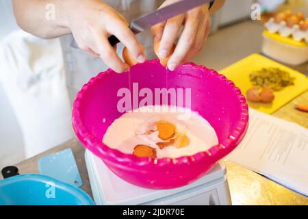 Der Prozess der Herstellung von handwerklichem Brot. Eier in die Milch für den Muffin-Teig geben. Vorderansicht. Stockfoto
