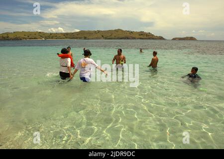 Menschen, die sich auf dem Küstenwasser eines Strandes, der aufgrund seines rosafarbenen Sandes auf der Komodo-Insel im Komodo-Nationalpark in Komodo, West Manggarai, East Nusa Tenggara, Indonesien, beliebt ist, entspannen. Stockfoto