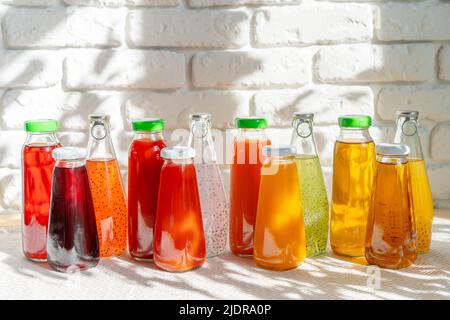 Reihe von Glasflaschen mit verschiedenen Säften gegen weiße Ziegelwände Stockfoto