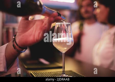 Details zur geringen Schärfentiefe (selektiver Fokus), bei denen Sekt an einer Bar in ein Glas gegossen wird. Stockfoto