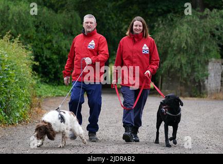 John Miskelly mit seinem Hund Bracken gemeinsam mit Teammitglied Emma Dryburgh und ihrem Hund Dougal führt John in seinem Haus in Falkland, Fife, ein spezialisiertes Hundeteam, das Leichen aufspüren und finden kann. Er und sein Team stehen bereit, um in der Ukraine zu helfen. Bilddatum: Dienstag, 21. Juni 2022. Stockfoto