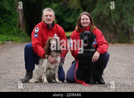 John Miskelly mit seinem Hund Bracken gemeinsam mit Teammitglied Emma Dryburgh und ihrem Hund Dougal führt John in seinem Haus in Falkland, Fife, ein spezialisiertes Hundeteam, das Leichen aufspüren und finden kann. Er und sein Team stehen bereit, um in der Ukraine zu helfen. Bilddatum: Dienstag, 21. Juni 2022. Stockfoto