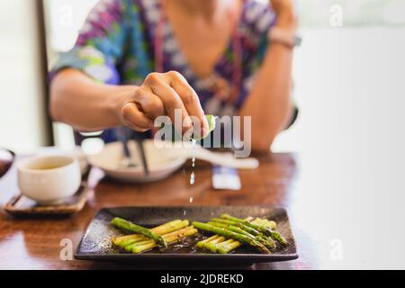 Weibliche Hand drückt Limette auf gekochten Spargel. Stockfoto