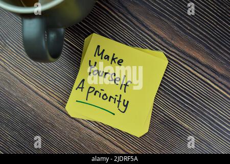 Das Konzept von Make Yourself A Priority Reminder schreibt auf Haftnotizen, die auf einem Holztisch isoliert sind. Stockfoto