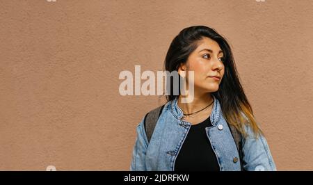 Nahaufnahme einer Latina-Dame mit jean-Jacke, die nach links blickt, mit einfarbigem Hintergrund dahinter Stockfoto