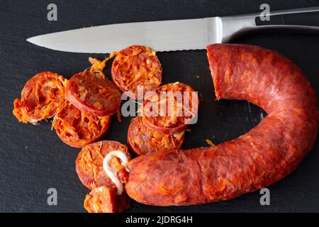 Spanischer Chorizo wurde mit einem Messer auf einem Schieferschneidebrett geschnitten. Stockfoto