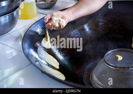 Ein Koch bereitet traditionelle nordöstliche Gerichte zu, Pfannkuchen, die in einer eisernen Pfanne geschmort werden Stockfoto