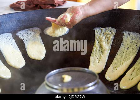 Ein Koch bereitet traditionelle nordöstliche Gerichte zu, Pfannkuchen, die in einer eisernen Pfanne geschmort werden Stockfoto