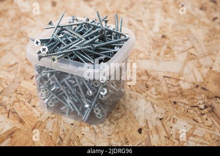 Kasten mit neuen glänzenden selbstschneidenden Schrauben steht auf einem Holzboden. Nahaufnahme des Hintergrundfotos mit selektivem Weichfokus Stockfoto