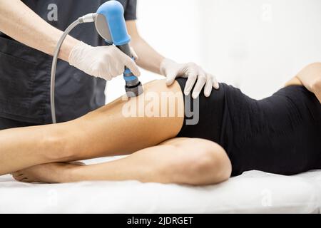 Der Arzt wendet eine Schockwellentherapie auf das Knie der Frau an Stockfoto