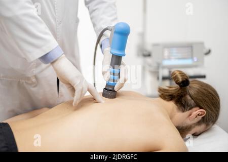 Der Arzt wendet eine Schockwellentherapie auf die Schulter des Mannes an Stockfoto