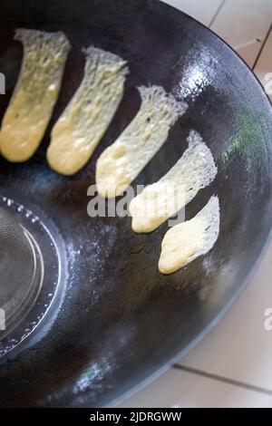 Ein Koch bereitet traditionelle nordöstliche Gerichte zu, Pfannkuchen, die in einer eisernen Pfanne geschmort werden Stockfoto