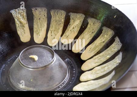 Ein Koch bereitet traditionelle nordöstliche Gerichte zu, Pfannkuchen, die in einer eisernen Pfanne geschmort werden Stockfoto