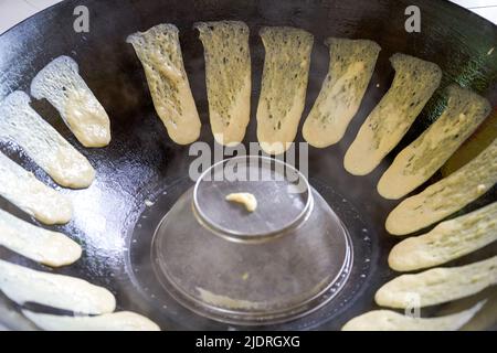 Ein Koch bereitet traditionelle nordöstliche Gerichte zu, Pfannkuchen, die in einer eisernen Pfanne geschmort werden Stockfoto