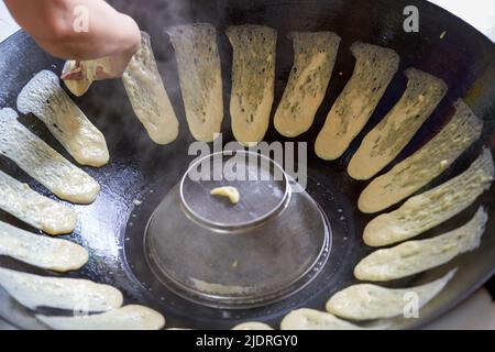 Ein Koch bereitet traditionelle nordöstliche Gerichte zu, Pfannkuchen, die in einer eisernen Pfanne geschmort werden Stockfoto