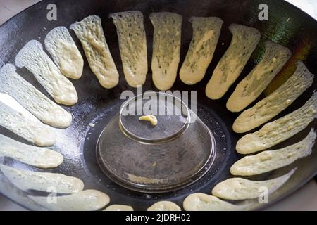 Ein Koch bereitet traditionelle nordöstliche Gerichte zu, Pfannkuchen, die in einer eisernen Pfanne geschmort werden Stockfoto