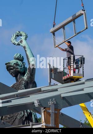 München, Deutschland. 23.. Juni 2022. Ein Arbeiter montiert Teile für ein Bierzelt auf dem Oktoberfest-Gelände. Im Hintergrund steht das Bayern, das über dem Wiesn-Gelände steht. Kredit: Peter Kneffel/dpa/Alamy Live Nachrichten Stockfoto