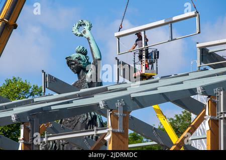 München, Deutschland. 23.. Juni 2022. Ein Arbeiter montiert Teile für ein Bierzelt auf dem Oktoberfest-Gelände. Im Hintergrund steht das Bayern, das über dem Wiesn-Gelände steht. Kredit: Peter Kneffel/dpa/Alamy Live Nachrichten Stockfoto