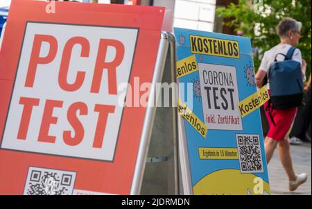 München, Deutschland. 23.. Juni 2022. Schilder mit den Aufschrift „PCR Test“ und „Corona Test - Free“ hängen vor dem Eingang einer Apotheke in der Innenstadt. Kredit: Peter Kneffel/dpa/Alamy Live Nachrichten Stockfoto