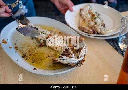 Serviert in einem Restaurant mit frischem gegrilltem Knoblauch und Olivenöl auf alten Kohleparrillas, Meerbarsch-Fisch im kleinen Fischerdorf Getaria, Baskisch Stockfoto