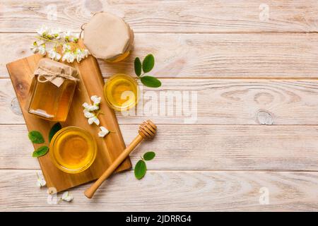 Honigglas mit Akazienblüten und Blättern auf Schneidebrett. Frischer Honig Draufsicht flach legen. Stockfoto