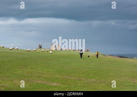 Northumberland Coast, Blick auf ein junges Paar, das auf dem malerischen Northumberland Coast Path zwischen Craster und Dunstanburgh Castle, England, Großbritannien, spazierengeht Stockfoto