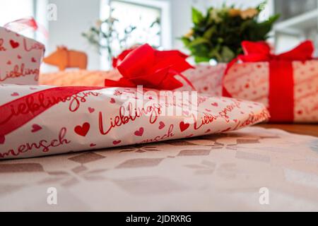 Liebevoller Geschenktisch mit roten und weißen Geschenken. Auf dem Geschenkpapier sind Herzen Stockfoto