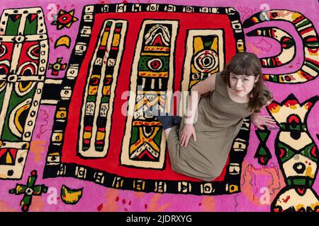 Edinburgh, Großbritannien. 23. Juni 2022 im Bild: Kuratorin Siobhan McLaughlin sitzt auf dem Gewehr getufteten Teppich, Celtic Spirit II. Die Dovecot Studios starten Alan Davie: Beginning of a Far-off World, eine Ausstellung zum hundertjährigen Bestehen des schottischen Künstlers Alan Davie (1920-2014). Diese Ausstellung zeigt selten gesehene Werke aus jedem Jahrzehnt seiner Karriere und ist eine Hommage an eine der großen Figuren der schottischen Kunst des 20.. Jahrhunderts. Die Ausstellung läuft vom 24. Juni bis zum 24. September 2022. Kredit: Rich Dyson/Alamy Live Nachrichten Stockfoto