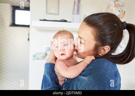 Mutter gibt ihrem Baby einen zarten Kuss auf die Wange für Zuneigung und mütterliche Liebe Stockfoto