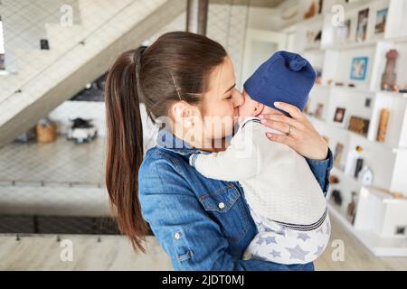 Glückliche Mutter mit Baby in den Armen gibt ihrem Säugling einen liebevollen Kuss Stockfoto