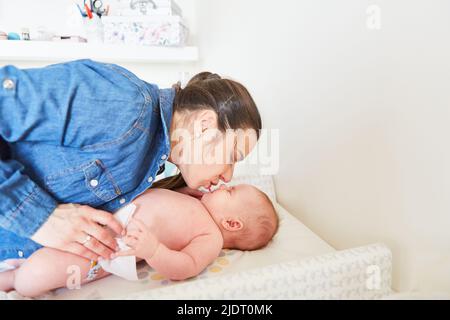 Mutter gibt ihrem Baby einen liebevollen Kuss auf dem Wickeltisch, während sie die Windel wechselt Stockfoto