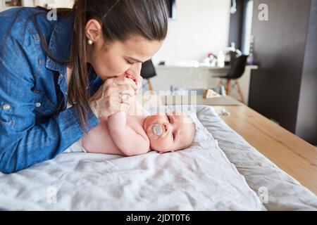 Die liebevolle Mutter gibt ihrem Baby einen Kuss, während sie die Windel auf dem Wickeltisch wechselt Stockfoto