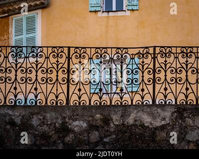 Abstraktes Muster, das von einem schmiedeeisernen Zaun mit einem alten Haus mit Fensterläden hinter ihm in einem provenzalischen Dorf im Südosten Frankreichs gebildet wurde. Stockfoto