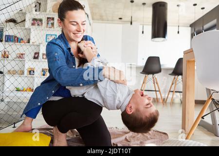 Mutter kitzelt ihren lachenden Sohn beim Spielen und Toben zu Hause im Wohnzimmer Stockfoto