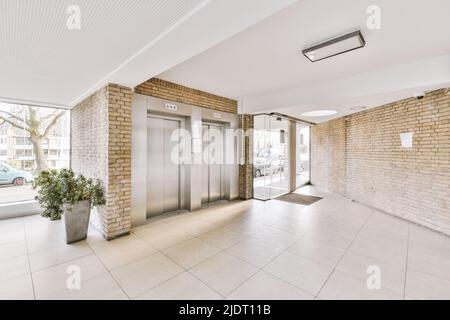 Glänzender Aufzug mit geschlossener Tür in der beleuchteten Halle des modernen Apartmentgebäudes mit Fliesenboden Stockfoto