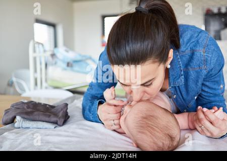 Glückliche Mutter gibt ihrem Baby einen Kuss, während sie die Windel auf dem Wickeltisch wechselt Stockfoto