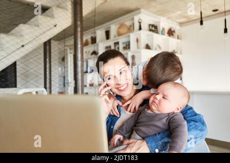 Die Mutter im Heimbüro telefoniert mit ihrem Smartphone und wird von Kindern abgelenkt Stockfoto