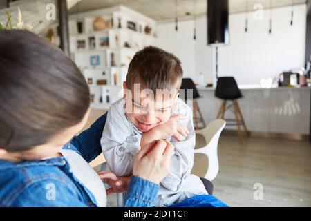 Mutter kitzelt ihren lachenden Sohn, während sie zu Hause im Wohnzimmer spielt Stockfoto