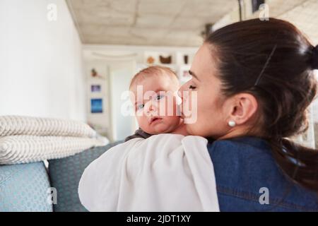Mutter gibt ihrem Baby zu Hause im Wohnzimmer einen zarten Kuss auf die Wange Stockfoto