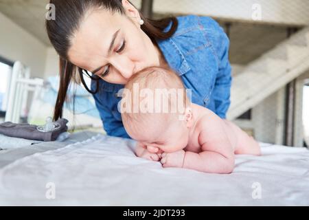 Mutter gibt ihrem neugeborenen Baby einen zarten Kuss, während sie die Windel wechselt Stockfoto