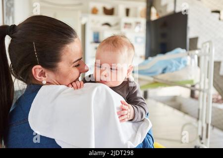 Glückliche Mutter hält ihr neugeborenes Baby zu Hause im Wohnzimmer liebevoll in den Armen Stockfoto