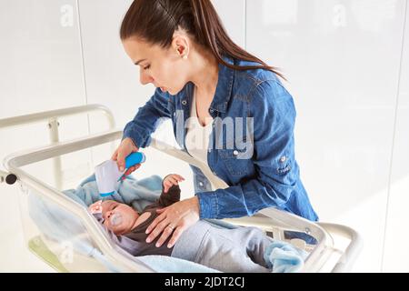 Mutter misst das Babyfieber im Bett mit einem berührungslosen Stirn-Thermometer Stockfoto