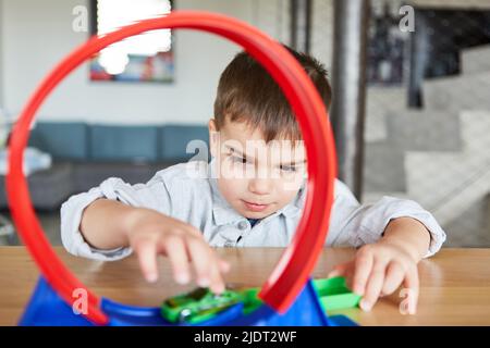 Boy spielt verträumt im Wohnzimmer mit Spielzeugrennbahn und Auto auf der Schleife Stockfoto