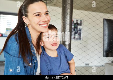 Der kleine Junge sitzt neben seiner Mutter und streckt seine Zunge als frech Junge aus Stockfoto