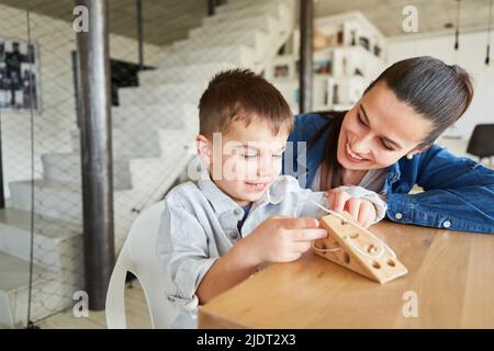 Junge, der mit seiner Mutter eine Schnur auf ein Holzspielzeug als Lernspiel einfädste Stockfoto