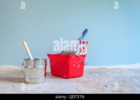 Hellblau lackierte Wand mit Malwerkzeugen vorne auf einem Betonboden Stockfoto