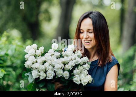 Frau hält Blumen großen Blumenstrauß weißen Blumen Rosen auf Dating in der Stadt. Blühende Blumen festlichen Hintergrund, Pastell und weichen Blumenstrauß Karte. Muttertag, Internationaler Frauentag. Stockfoto