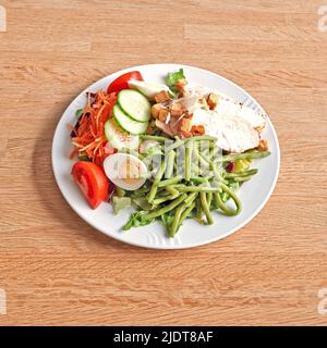 Weißer Teller mit einem Caesar-Salat auf einem Holztisch Stockfoto