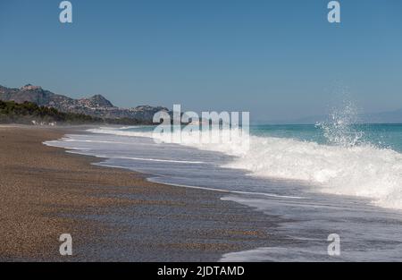 Brechende Wellen am schönen Strand von Fondachello, Sizilien, Italien. Die beliebten Städte Taormina und Giardini Naxos liegen in der Ferne Stockfoto